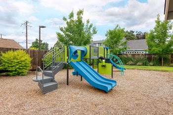 a playground with a blue slide and chairs in a yard at Trillium Apartments, Oregon